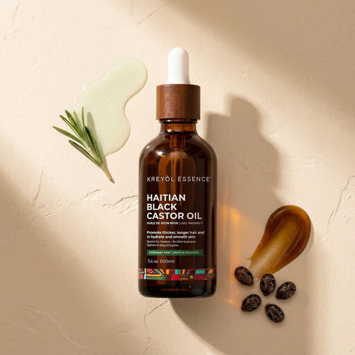 Kreyòl Essence Haitian Black Castor Oil with rosemary and peppermint in a 3.4oz bottle, shown in flatlay with botanical elements.