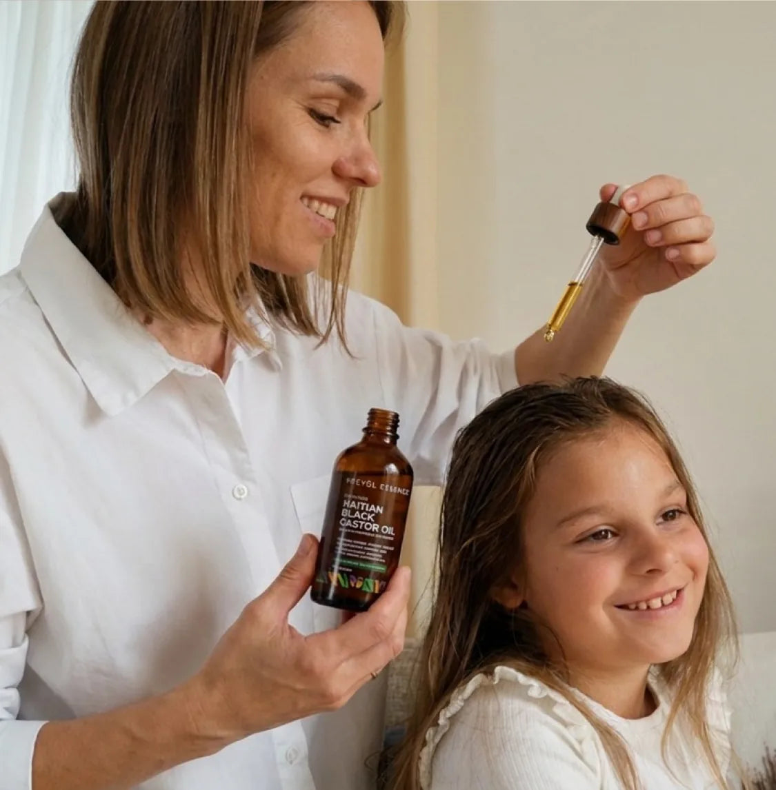A parent applying Haitian Black Castor Oil to a child's hair with a dropper