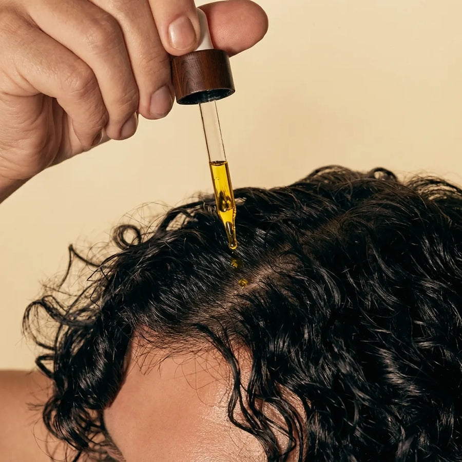 A dropper applying Haitian Black Castor Oil to the scalp of curly hair