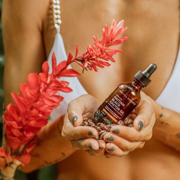 Haitian Black Castor Oil by Kreyòl Essence with mango, papaya, and coconut, shown in a clear bottle with natural ingredients.